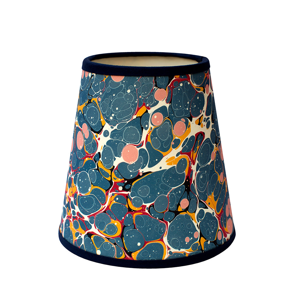 A dark blue paper lampshade with a pink, red and orange marbled design and a navy velvet trim.