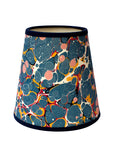 A dark blue paper lampshade with a pink, red and orange marbled design and a navy velvet trim.
